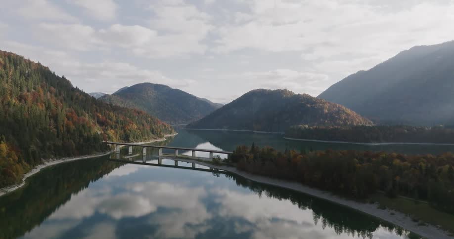Bridge over a lake reflecting mountains and clouds in the background