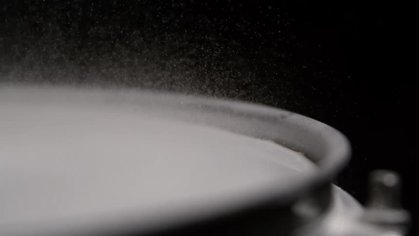 A drumhead vibrates and lifts a fine cloud of powder into the air