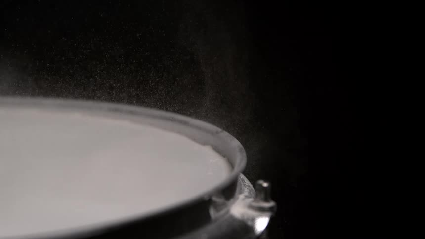 Fine white dust rises from the white surface of a metal container