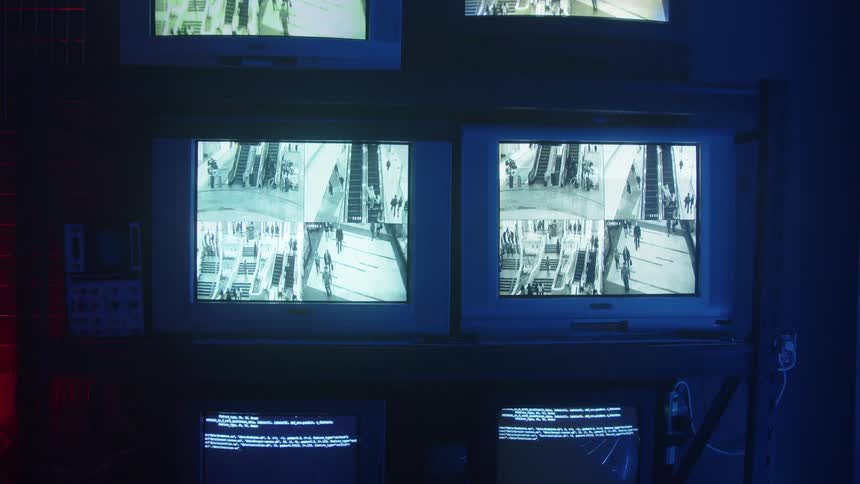 Multiple monitors sitting on a shelving unit display text and videos in a room lit by colored lighting
