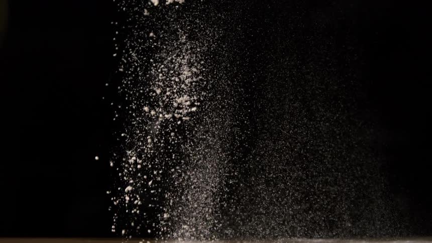 Flour falls in a fine cloud against a dark background forming suspended particles