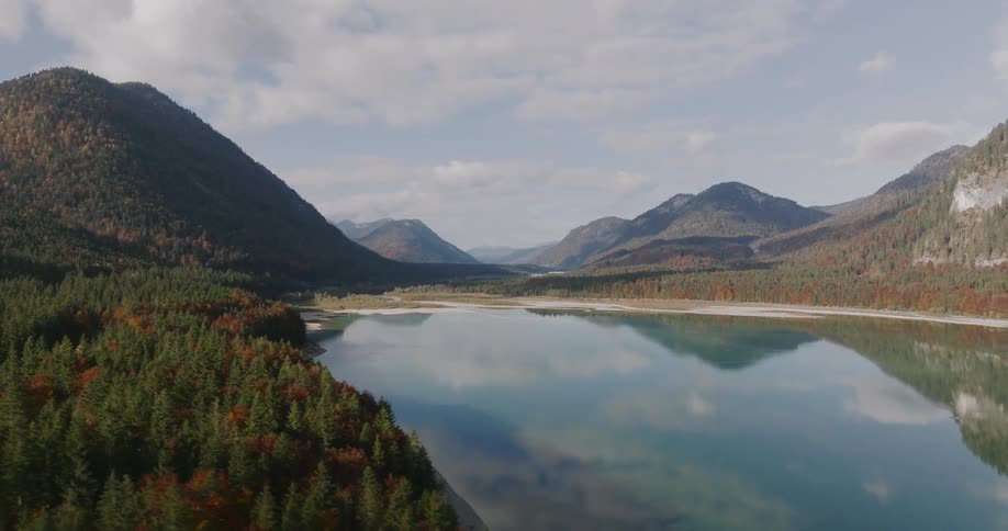 Aerial view of a calm lake reflecting mountains and forests under a cloudy sky