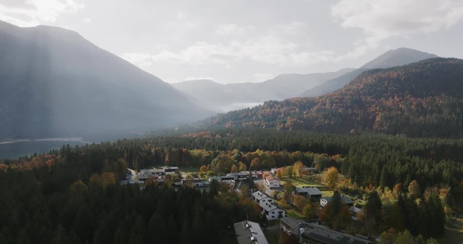Aerial view of a mountain town nestled in a forested valley beneath sunlit peaks