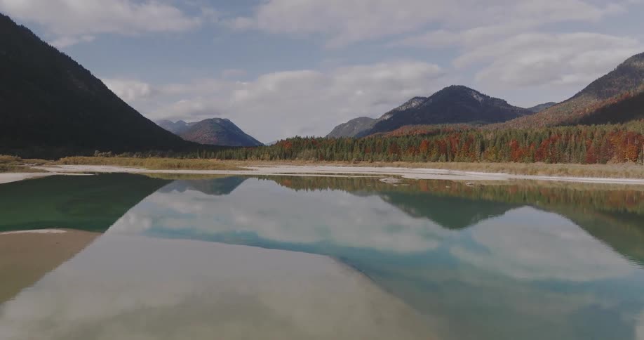 A landscape of a lake reflecting mountains and the vegetation of a pine forest in the background