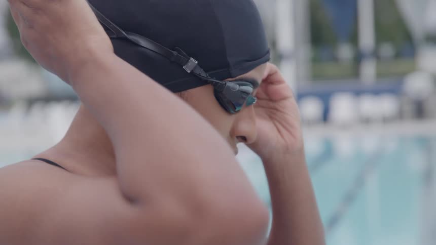 A woman is adjusting her swim goggles as she stands next to a pool
