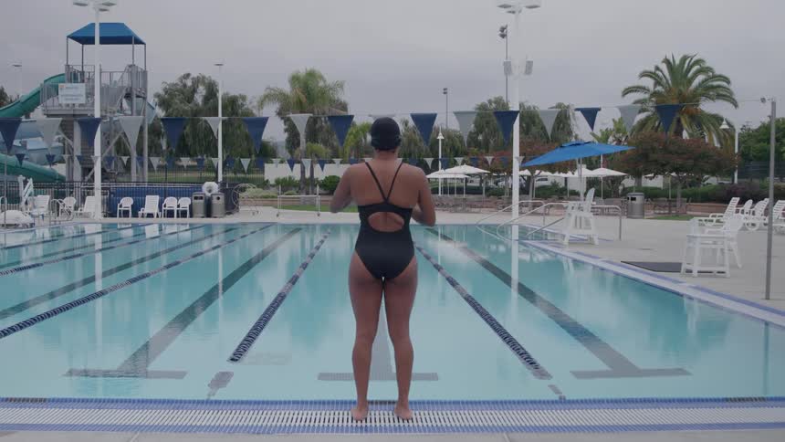 A young black woman preparing to swim while standing in front of an outdoor pool during daytime