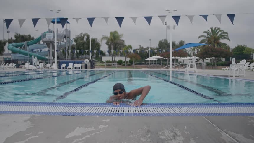 A swimmer practices in an outdoor pool on a cloudy day