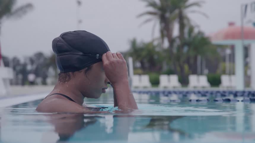 Female swimmer pulls down her goggles while preparing to swim in an outdoor swimming pool on a summer day