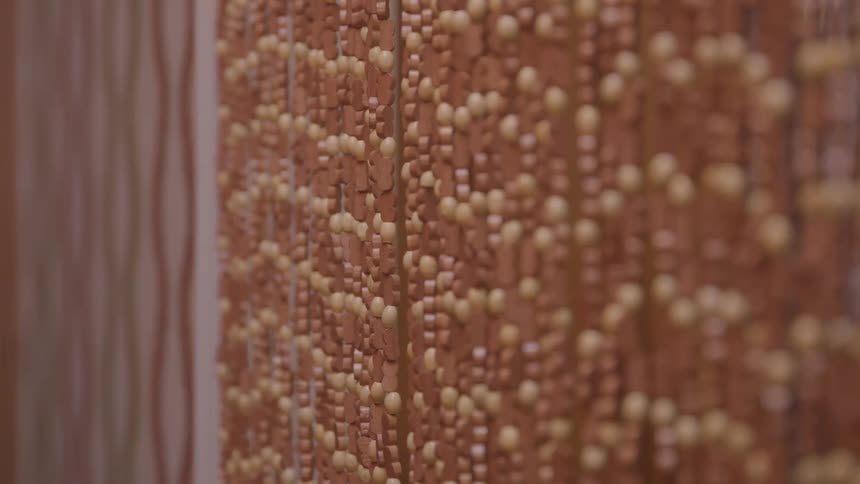 Curtain of brown and tan beads sways in an indoor doorway
