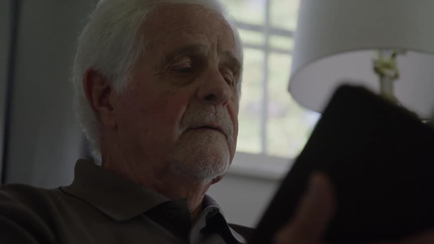 Elderly man reading a book indoors near a window