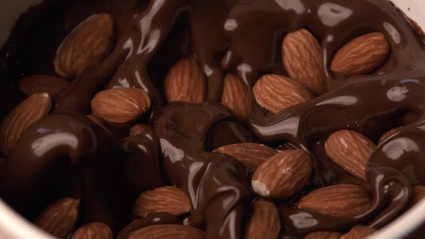 A closeup of almonds dropping into a bowl of melted chocolate