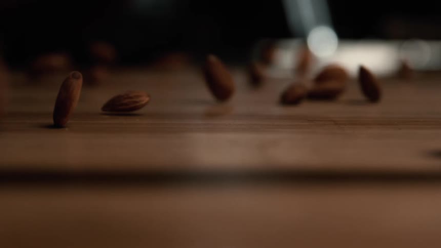 A closeup of almonds falling and bouncing across a wooden surface