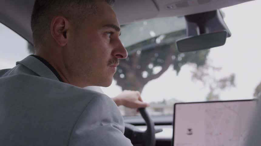 A man in a gray suit drives a car while focusing on the road ahead
