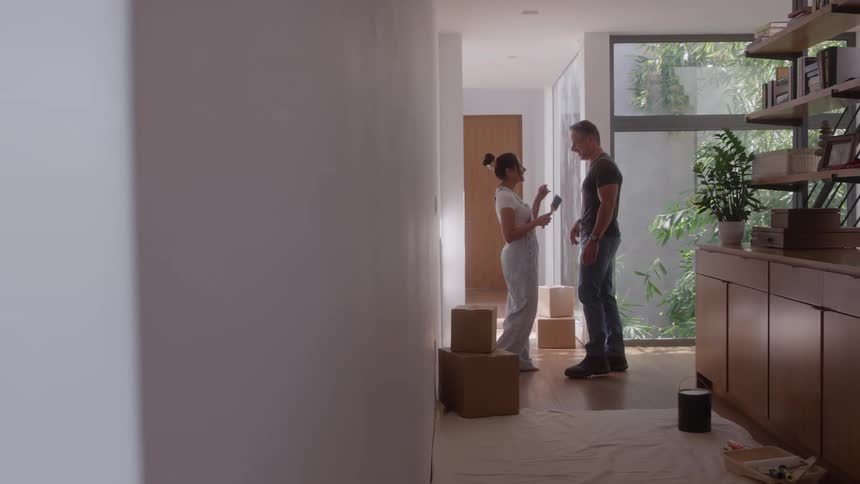 A couple talks and smiles in a modern entryway with moving boxes and paint supplies
