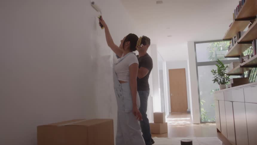 A couple paints a white wall together inside a bright modern home