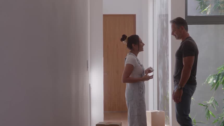 Woman teases her husband with a paintbrush while standing in their home