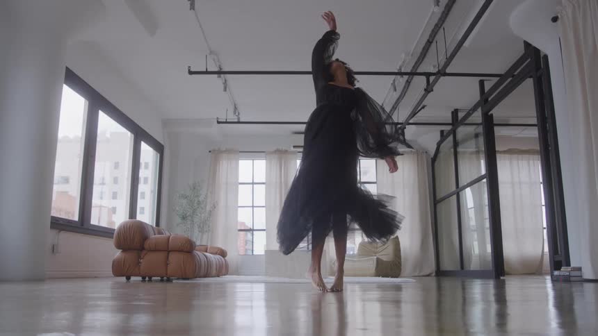 A woman wearing a black dress dancing and spinning in the middle of the room