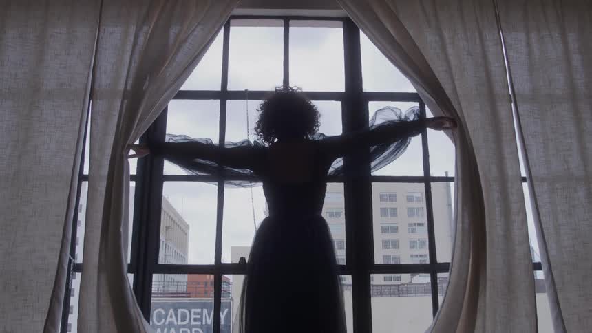 A woman in a gown is dramatically pulling the curtains apart in a window