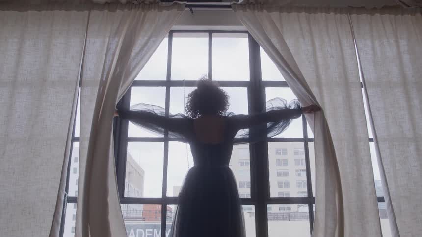 The woman opens the curtains on the window