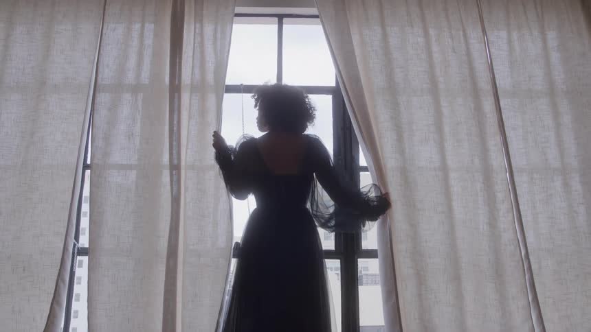 A woman standing in front of a window holding the curtains