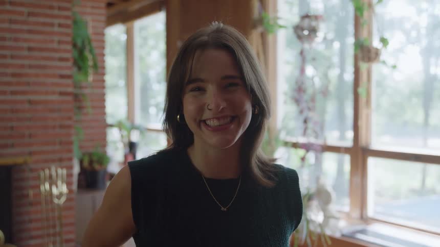 A young woman smiles warmly in a bright sunlit room