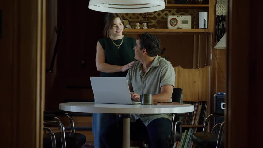A couple smiles and talks while looking at a laptop in a cozy wooden room
