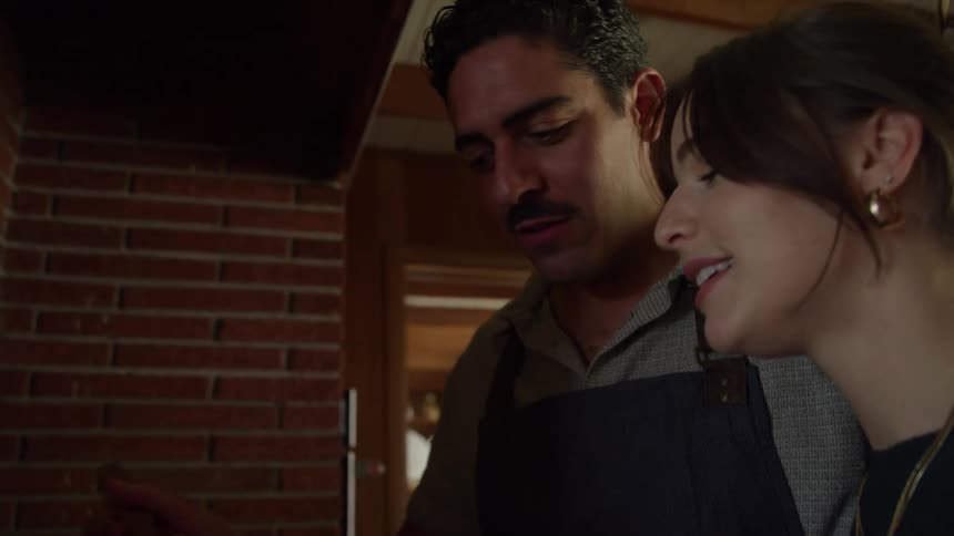 A woman walks into a kitchen to a man who is cooking and he offers her a taste