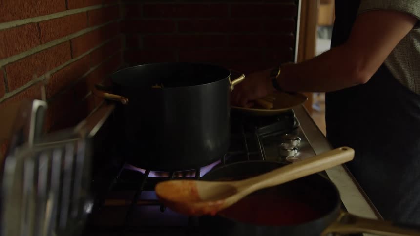 A person stirs sauce in a pot on a stove in a warm kitchen