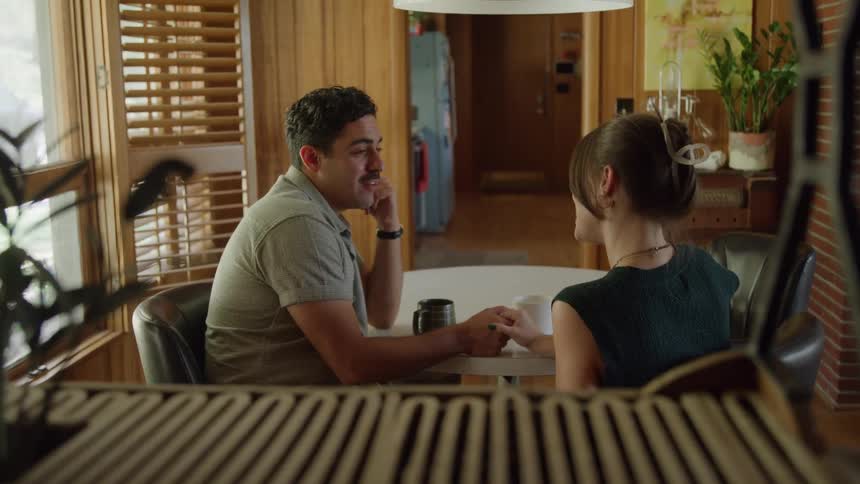 A man and woman smile warmly and hold hands over coffee in a cozy room