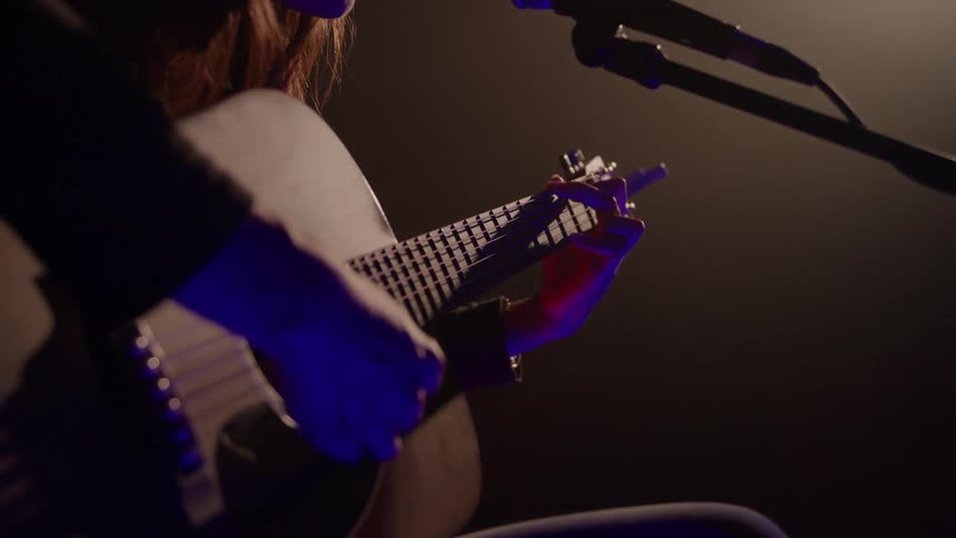 A person plays an acoustic guitar on stage under warm and blue lighting