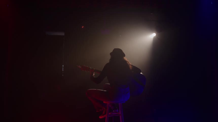 The woman plays the guitar under the spotlight