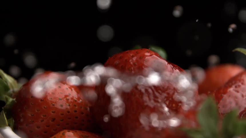 Close up of crystal clear water splashing on red ripe strawberries