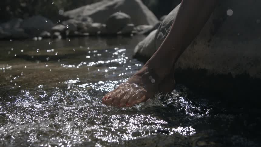Feet touch the stream water creating splashes lit by natural light
