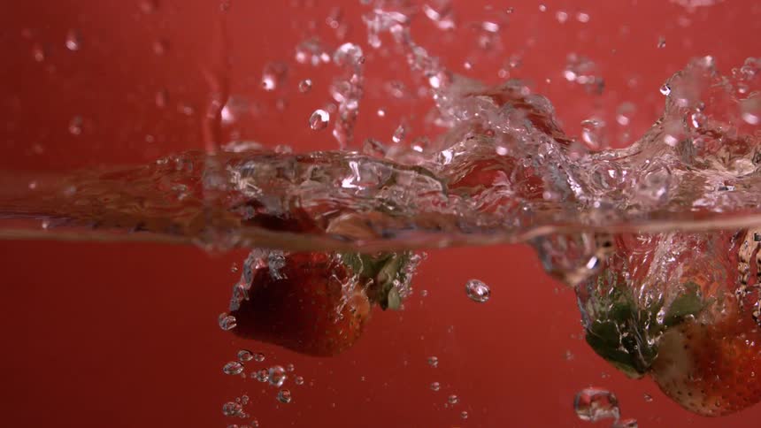 Several strawberries are dropped into clear water and become submerged