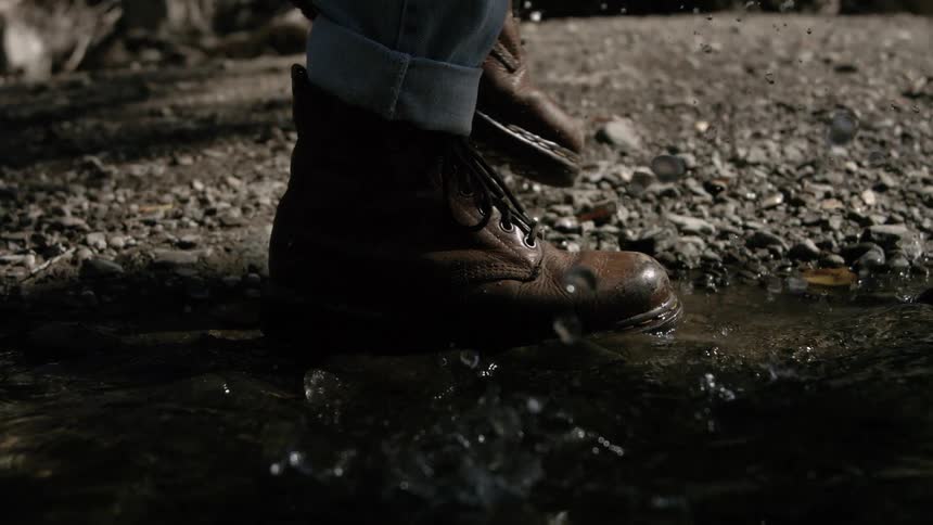 A person wearing boots steps into a puddle of water causing a splash at midday