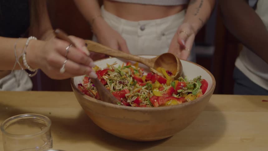 Hands toss a colorful salad in a wooden bowl on the table