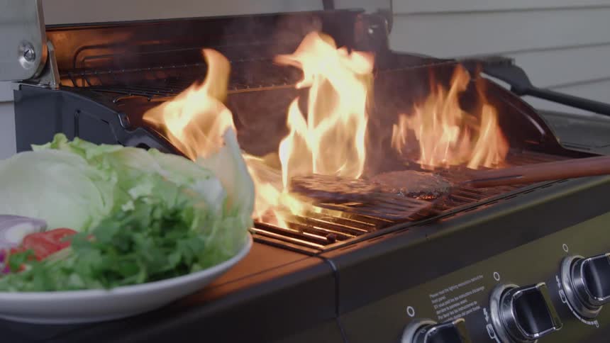 Intense flames grill burgers as fresh vegetables wait to assemble the sandwiches