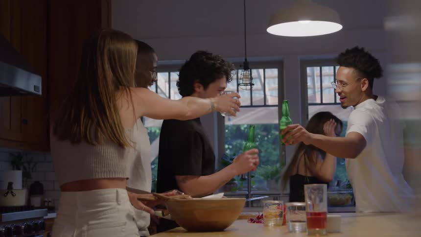 Friends toast and prepare food together in a brightly lit kitchen