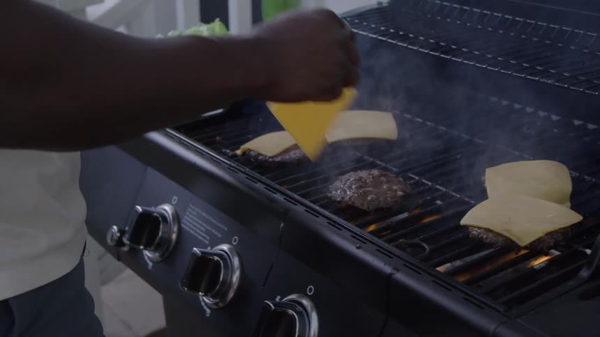 Person places slices of cheese on burgers grilling on the barbecue