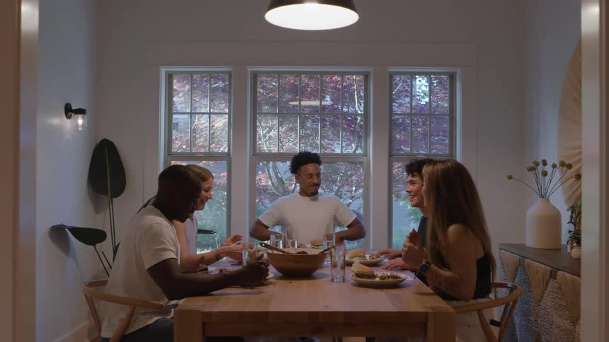 Five people gathered around a table laden with food are praying with their eyes closed and then they begin to smile