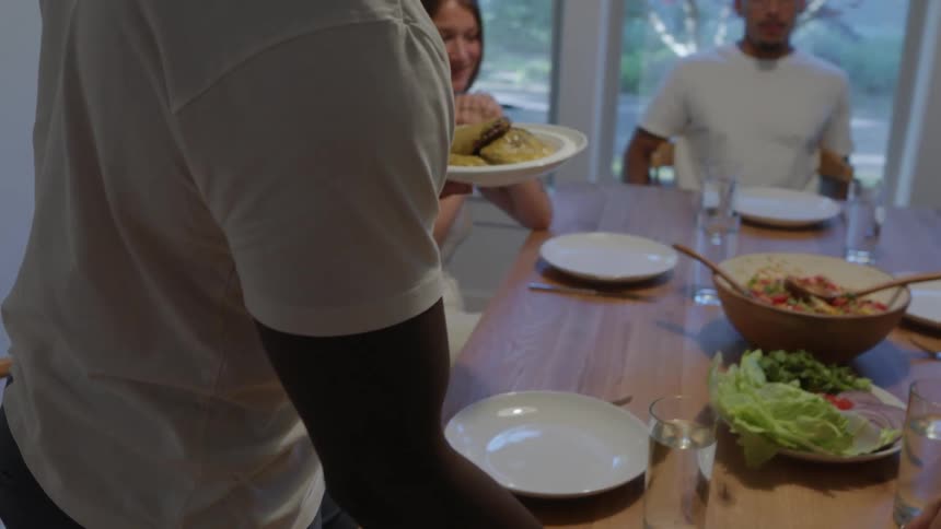 Person places a bowl of salad on the table as friends get ready to eat