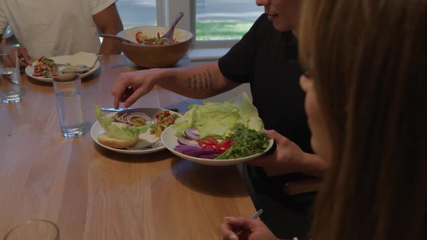 Person assembles a burger with lettuce onion and bell pepper on the table
