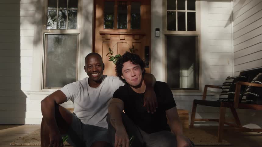 Two young men sit on the front porch holding beer bottles