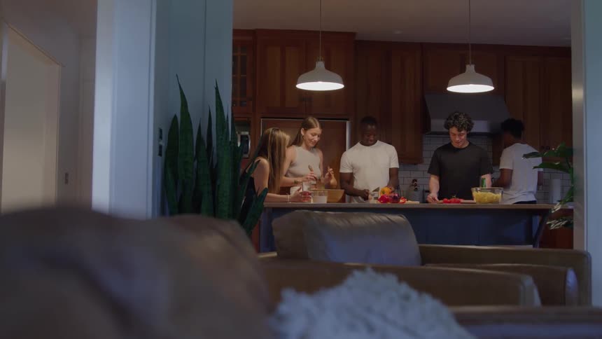 Five people are gathered around a table preparing a meal while chatting