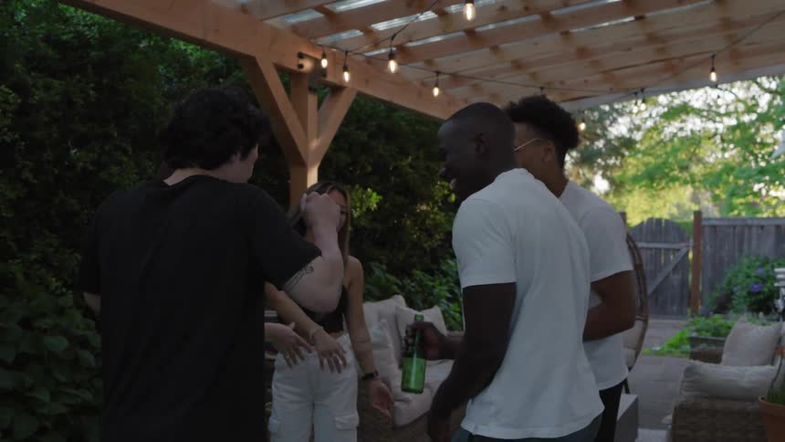 Friends dance and laugh around a fire pit at an evening patio party