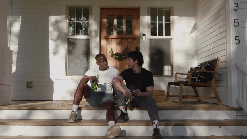 Two friends talk while sitting on the porch with bottles in hand