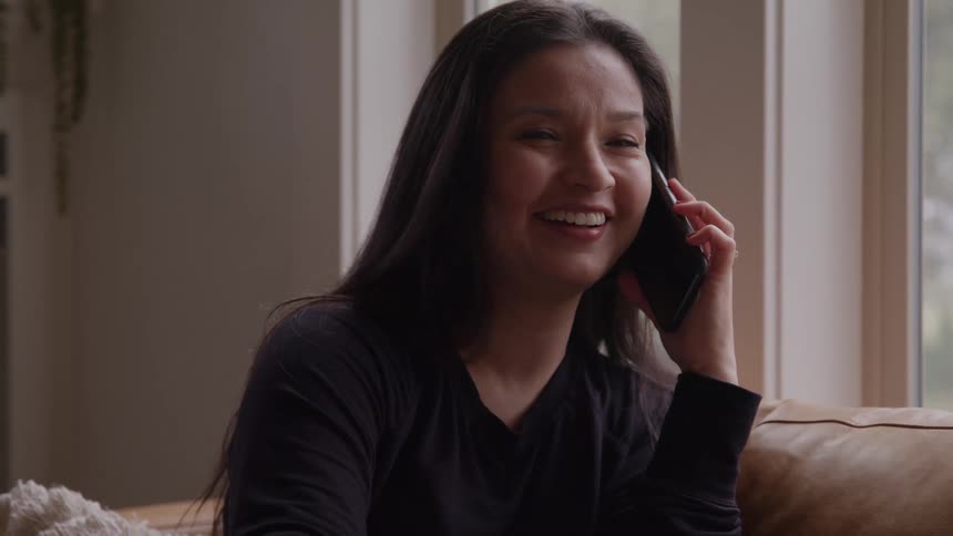 The face of a woman smiling while talking on a phone near a window