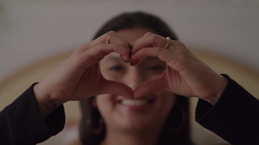 Young woman smiles as she makes a heart shape with her hands