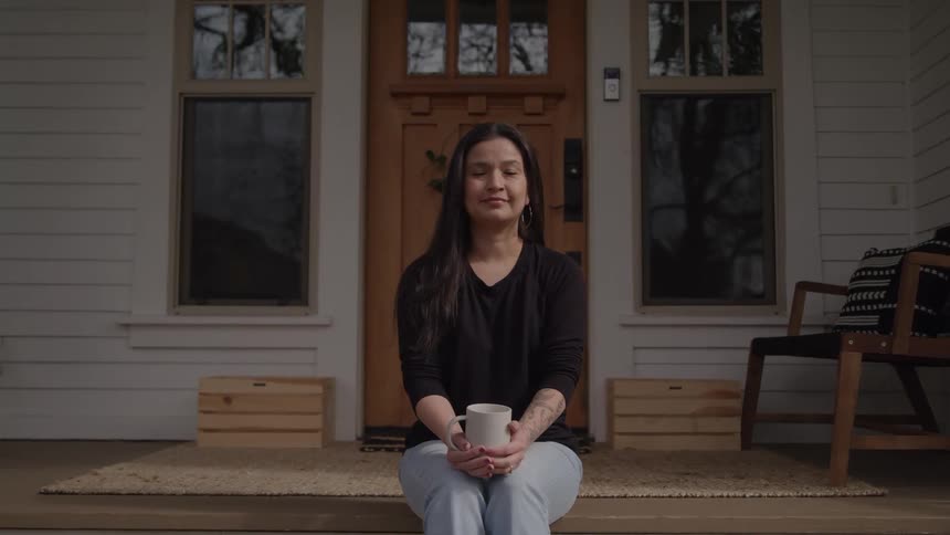 Woman sits on the porch steps holding a mug and looking ahead