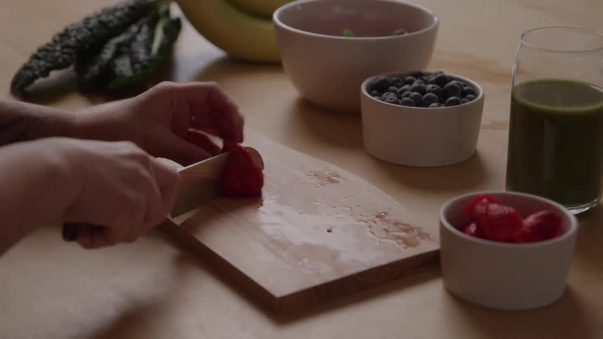 Woman standing at the kitchen counter slicing strawberries and placing them in a cup